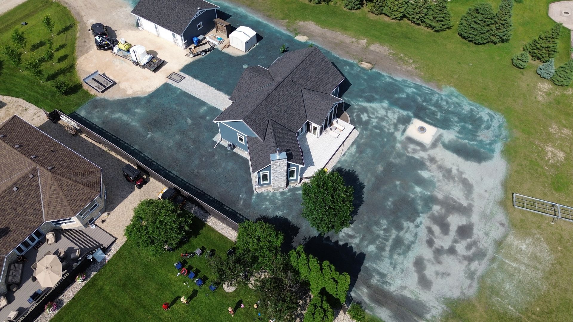 Aerial view of a blue house with a dark roof on a grassy property; areas of the lawn appear newly seeded