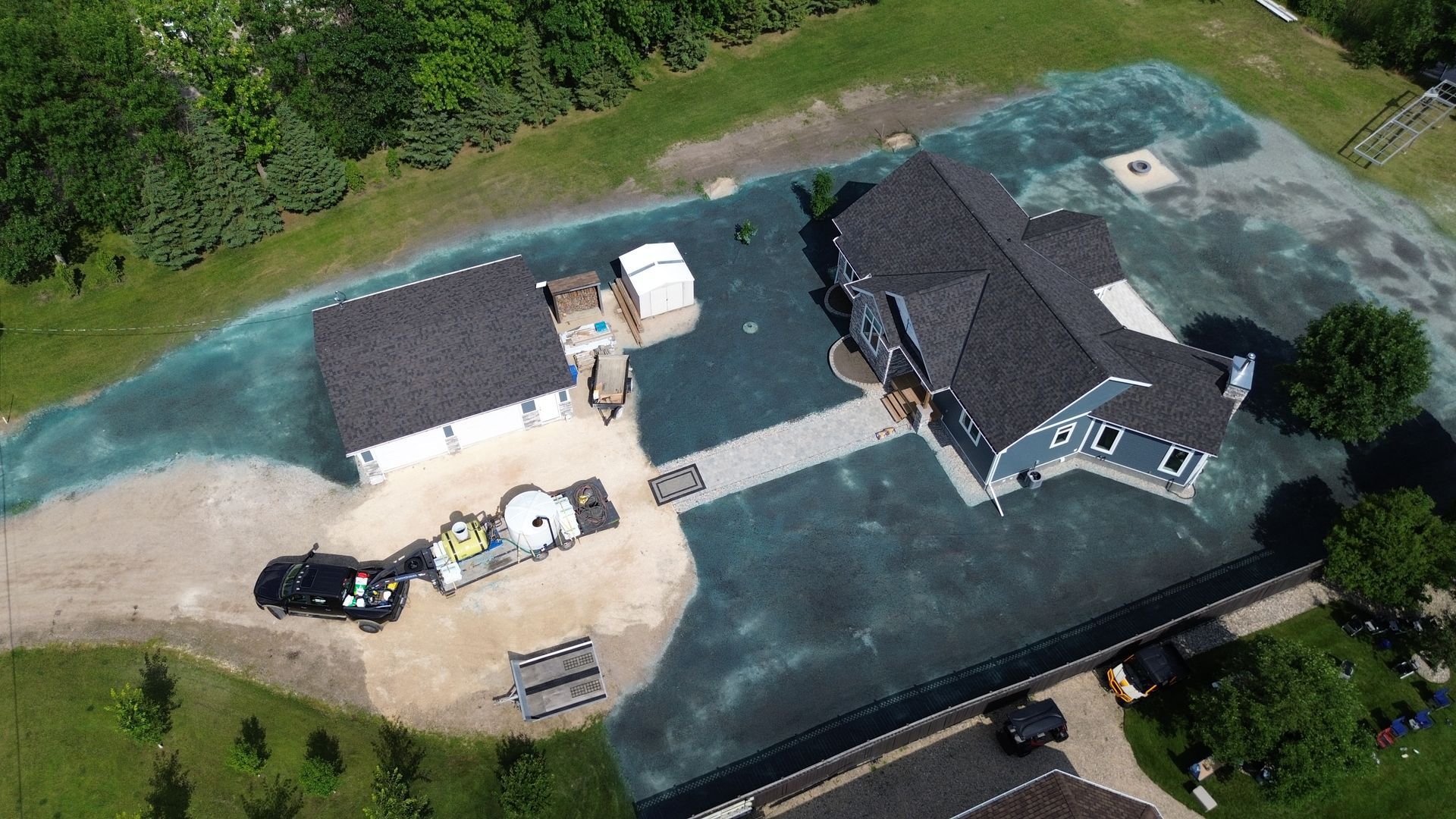 Aerial view of a house and garage with blue-treated lawn, landscaping, and a vehicle parked in the driveway.