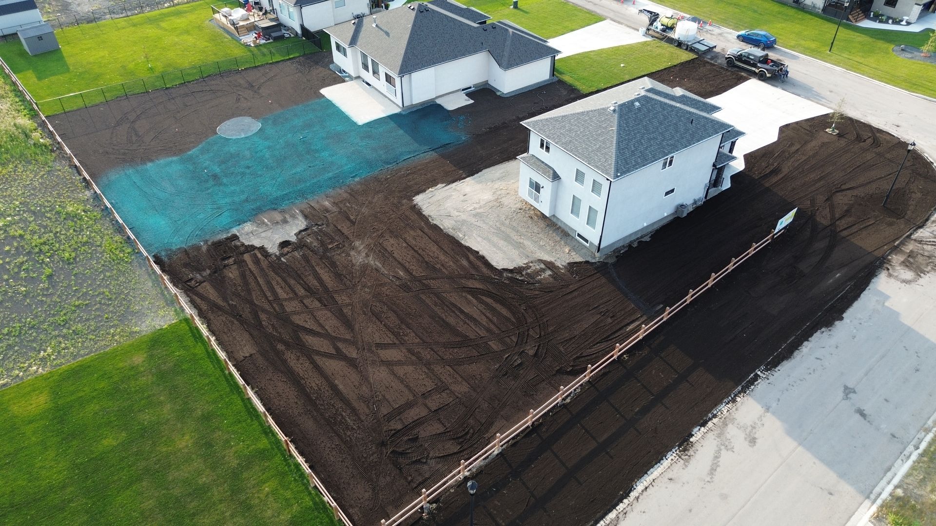 Aerial view of new houses under construction, with dark soil, green grass, and blue netting.