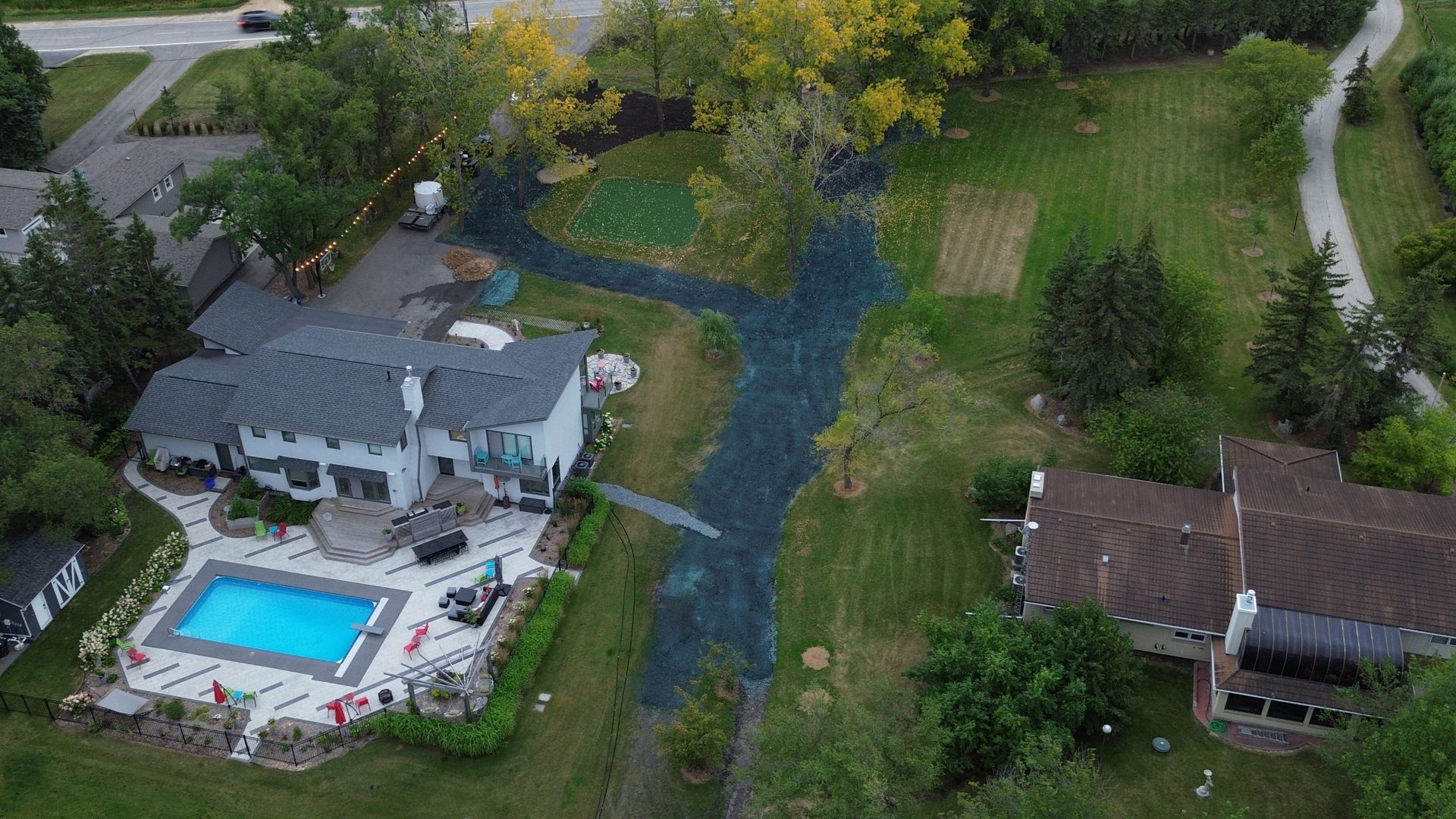 Aerial view of two houses with driveways, trees, and a swimming pool. new landscaping