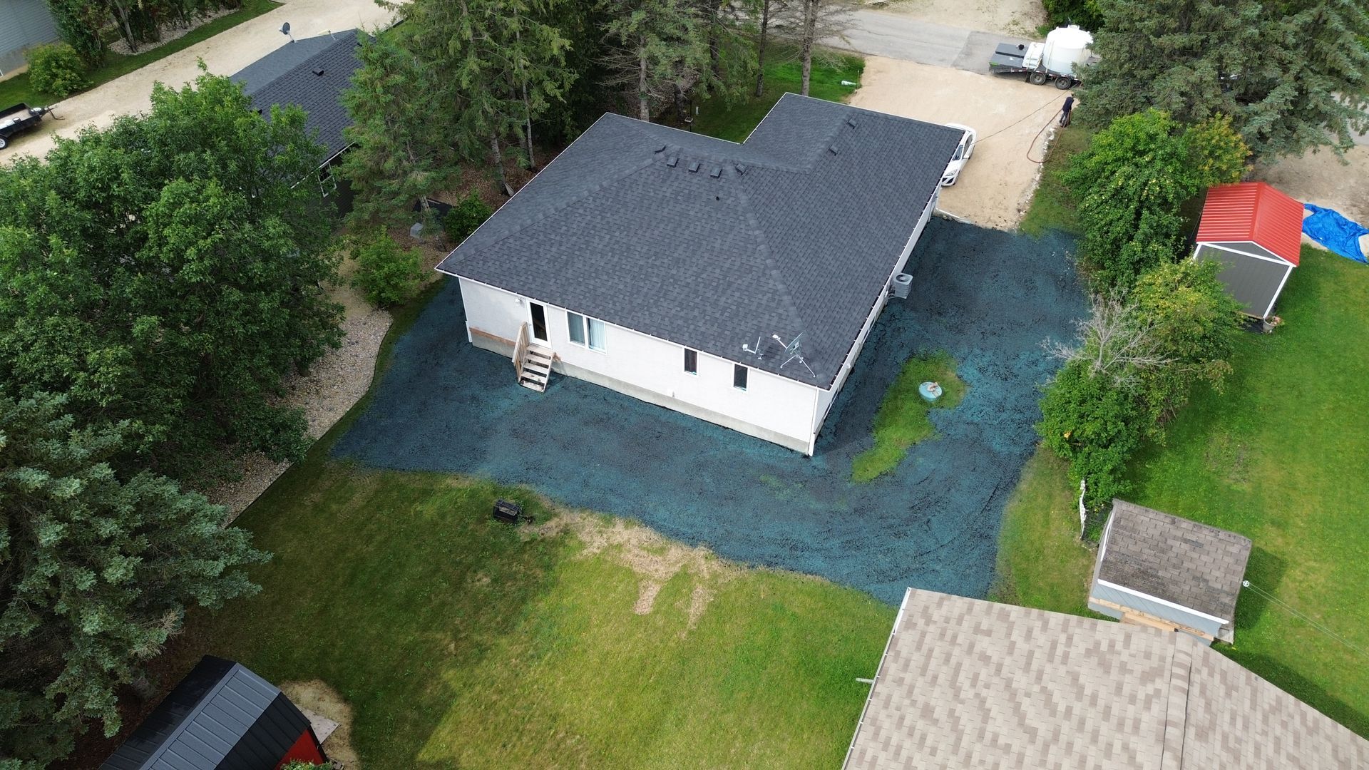 Overhead view of a white house with a dark roof and a gravel driveway surrounded by green grass and trees.