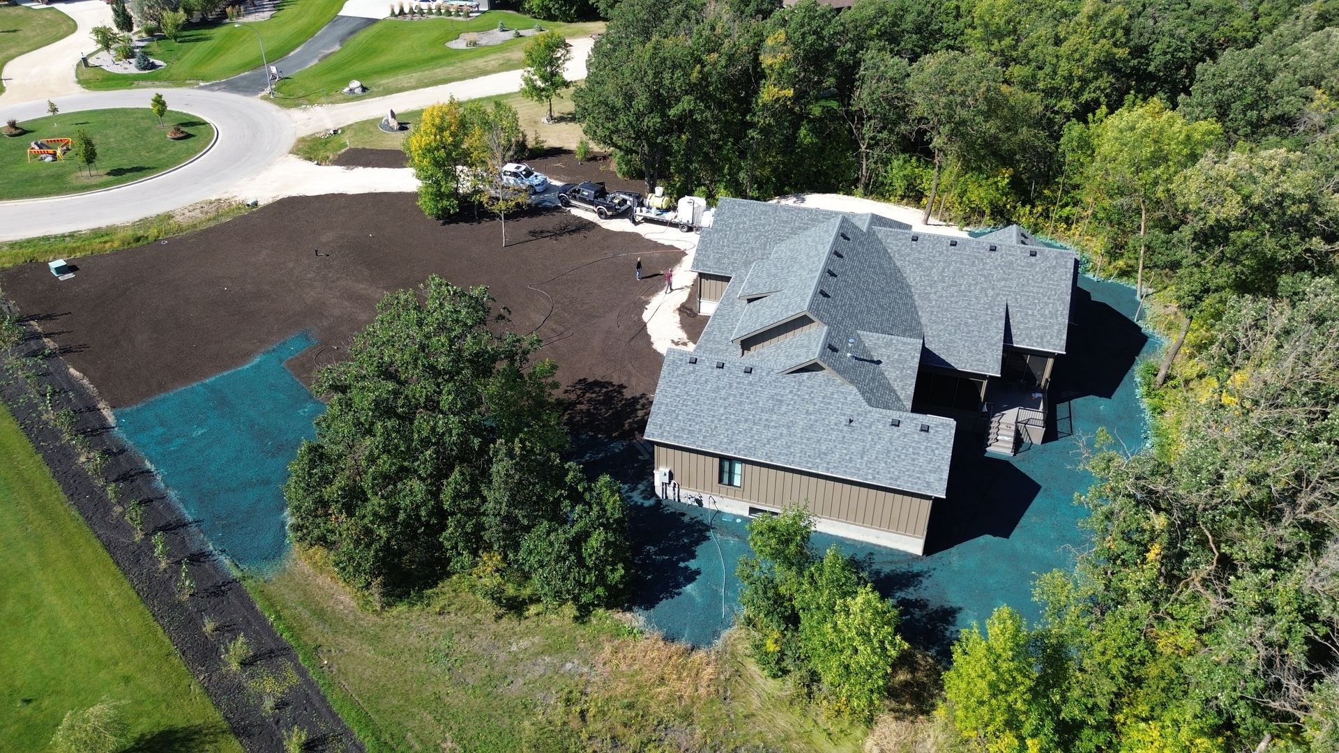 Aerial view of a brown house with a dark gray roof surrounded by trees and newly laid sod.