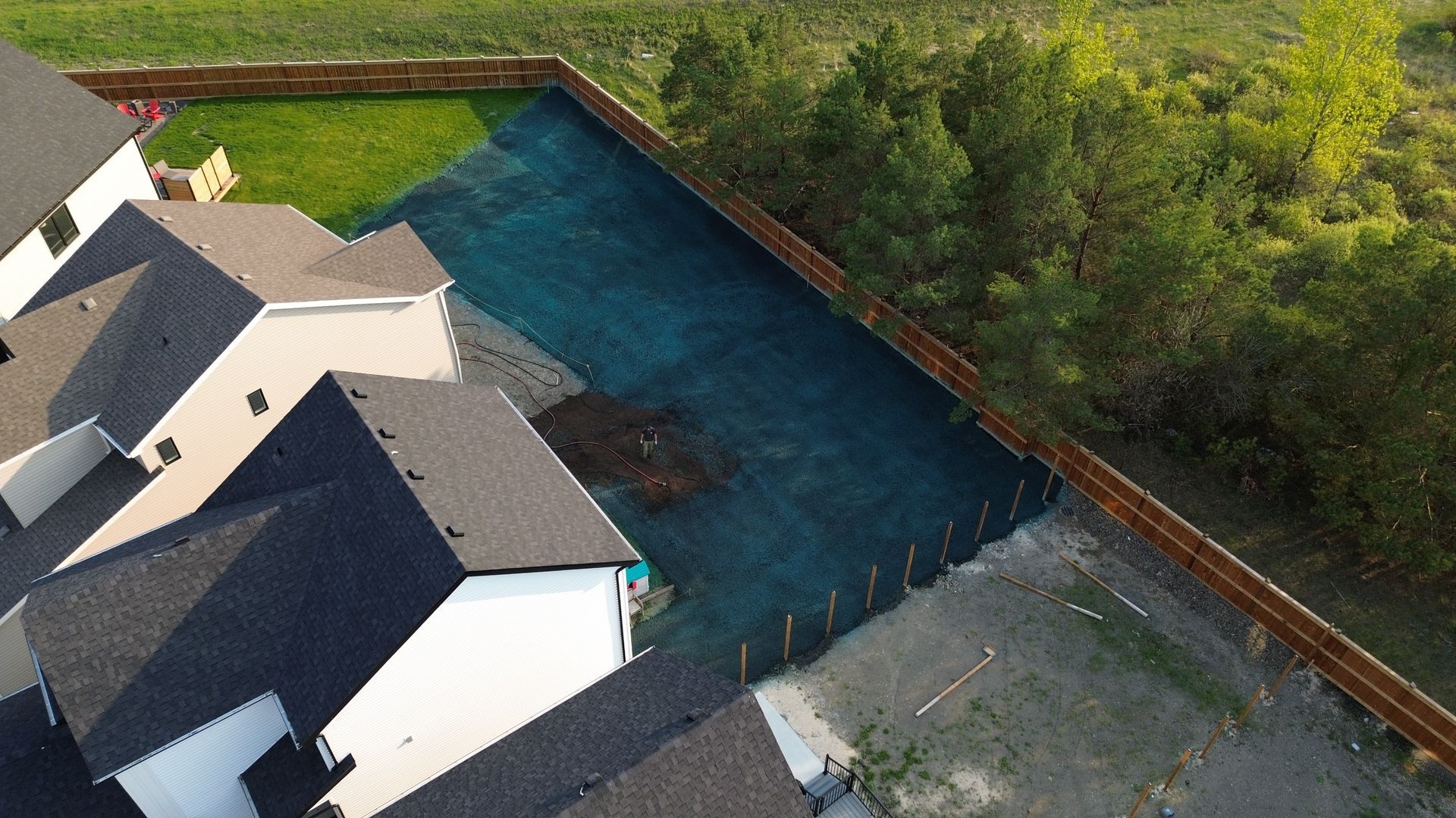 Aerial view of a home with dark roof, next to a backyard with newly laid grass and a wooden fence.