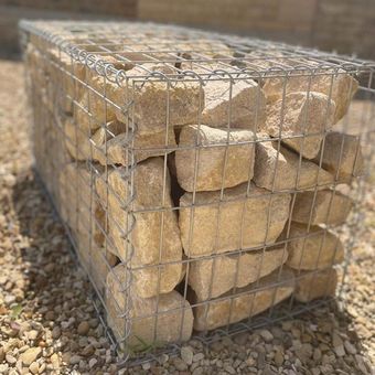 Gabion basket filled with beige stones, set on gravel.