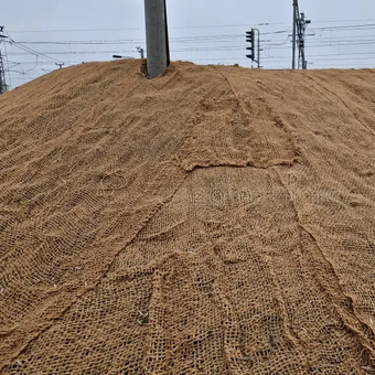 Brown erosion control blanket covering a dirt embankment near power lines.