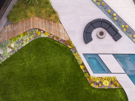 Landscaped garden border with stones, colorful flowers, and a wooden deck beside green lawn