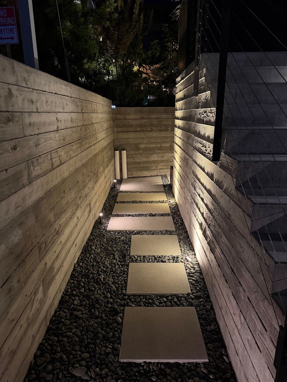 Narrow illuminated walkway between tall concrete walls with square stepping stones at night