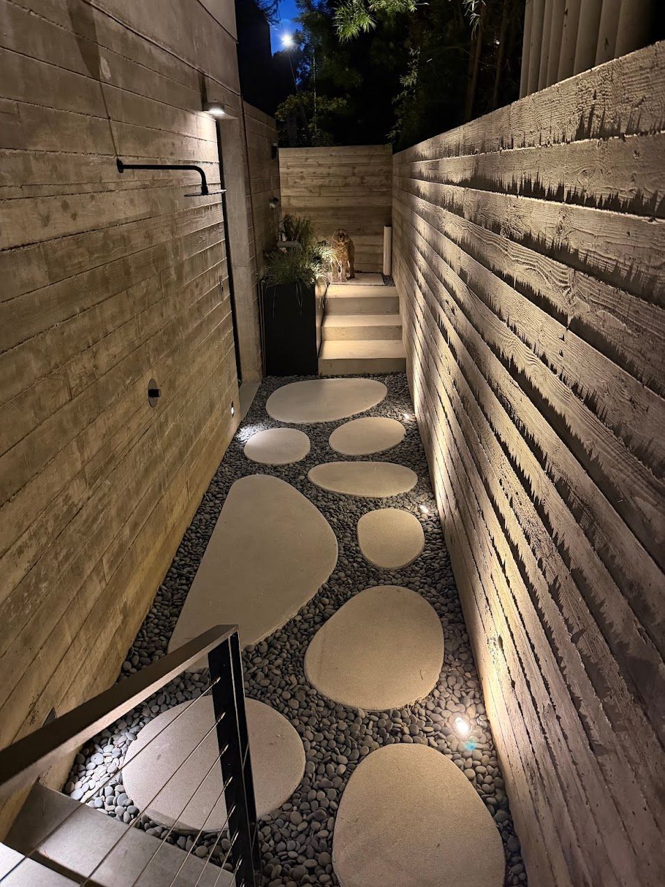 Narrow lit stone walkway with circular stepping stones between tall walls at night