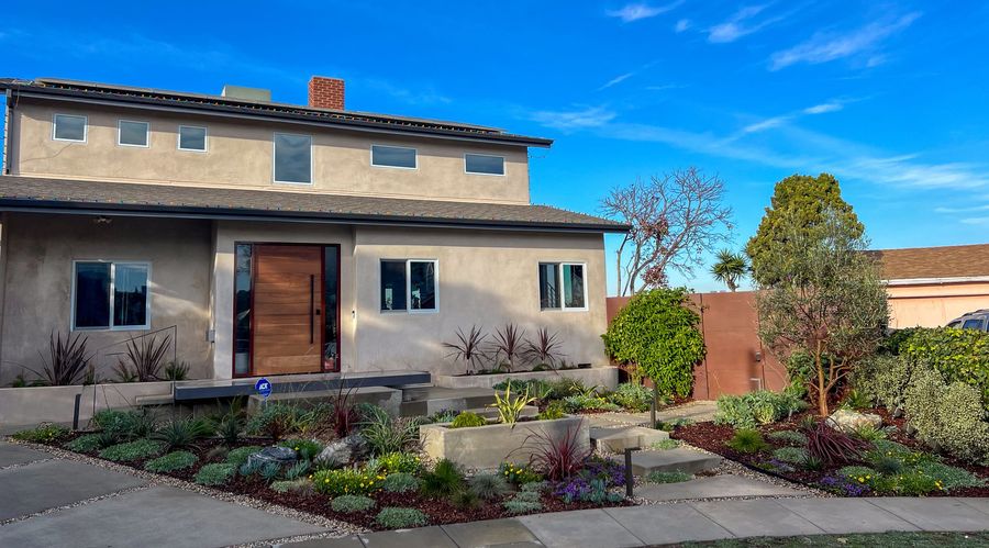 Front view of a beige stucco house with a landscaped garden and clear blue sky