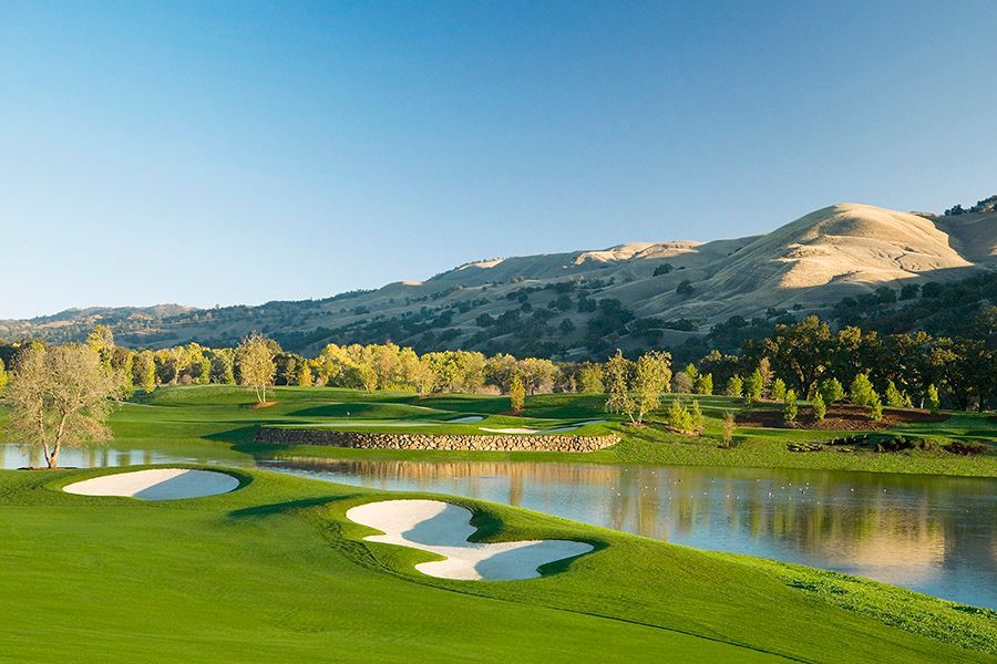 a golf course with a lake and mountains in the background