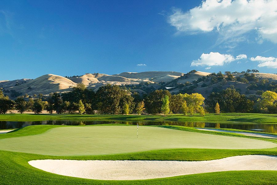 a golf course with a lake in the middle of it and mountains in the background