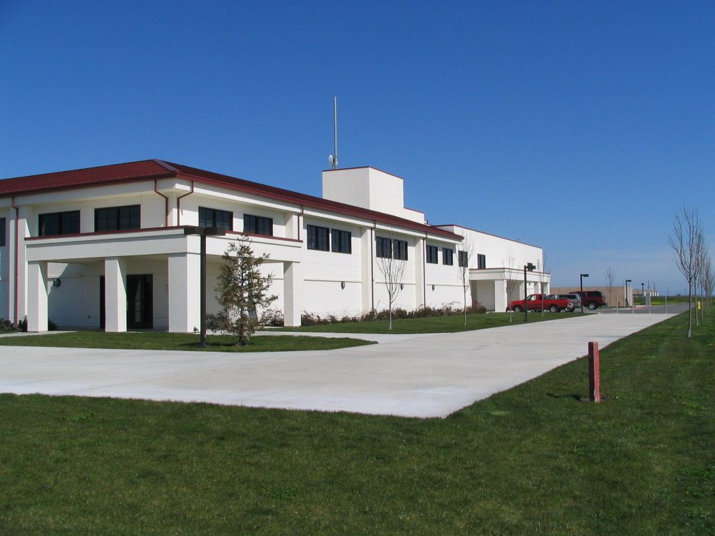 a large white building with a red roof is sitting on top of a lush green field