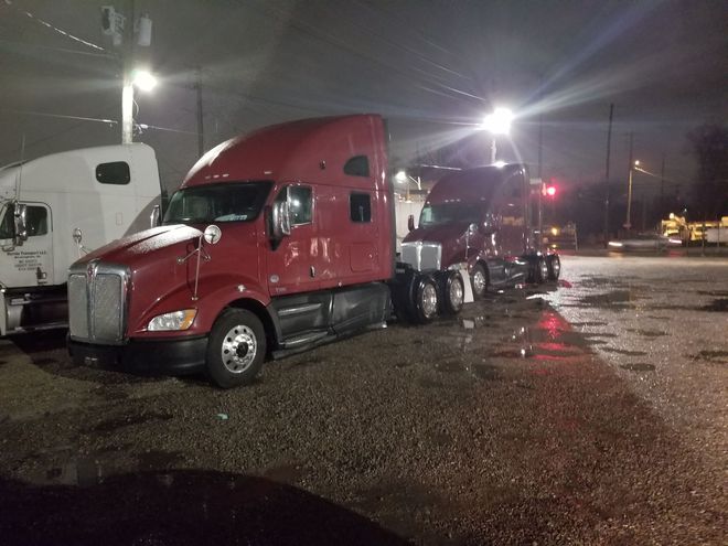 Two semi trucks are parked in a parking lot at night.