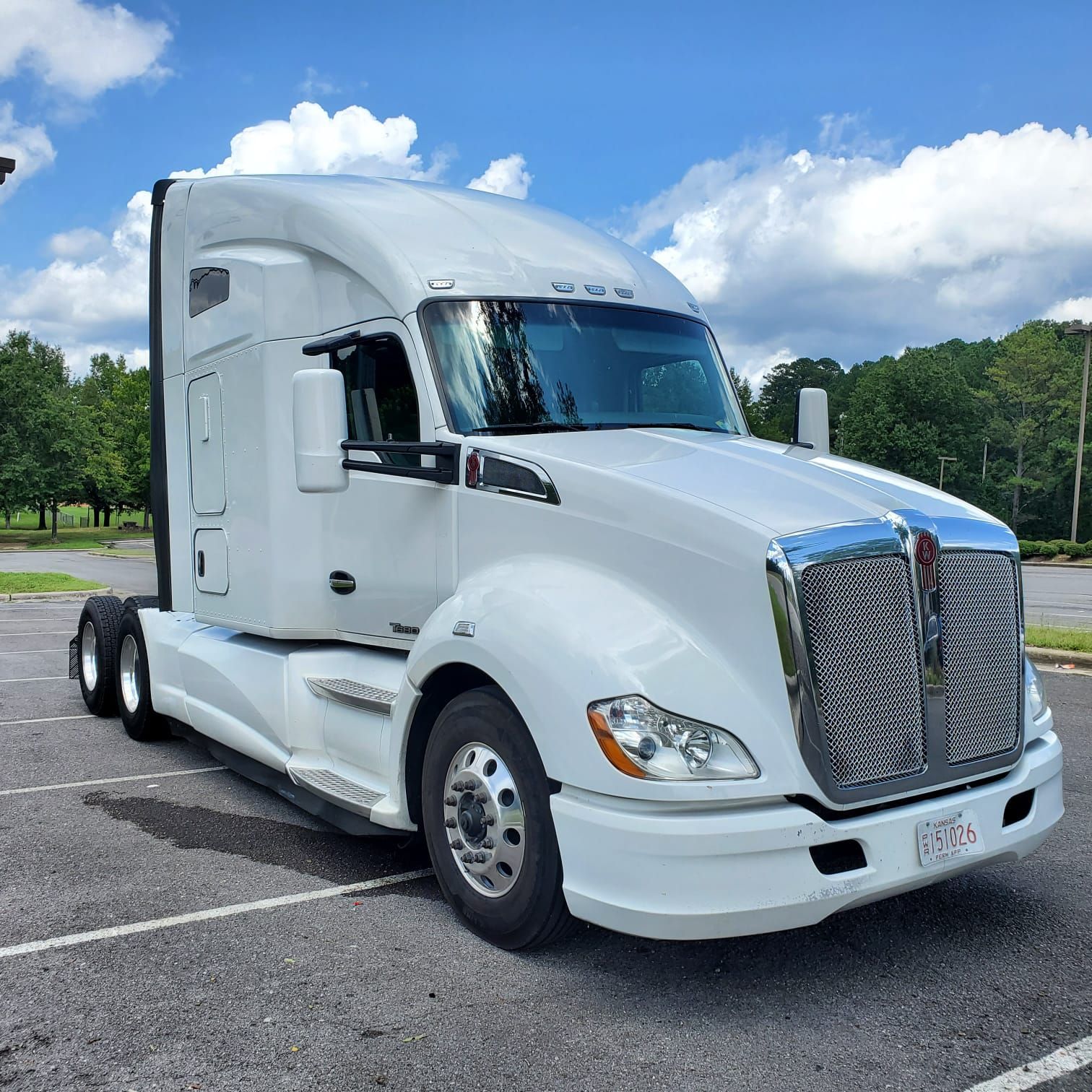 White semi-truck parked outdoors on a paved lot under a partly cloudy sky
