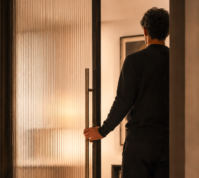 Person opening a frosted glass door in a softly lit hallway