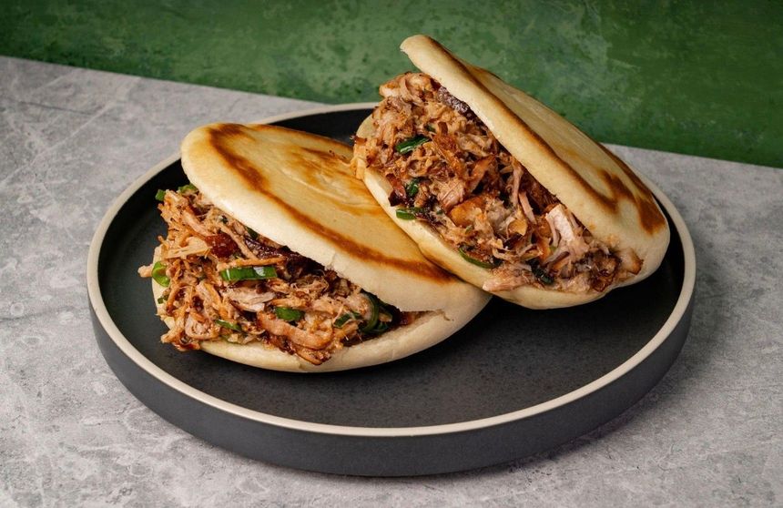 Two stuffed pita sandwiches on a black plate against a gray and green background