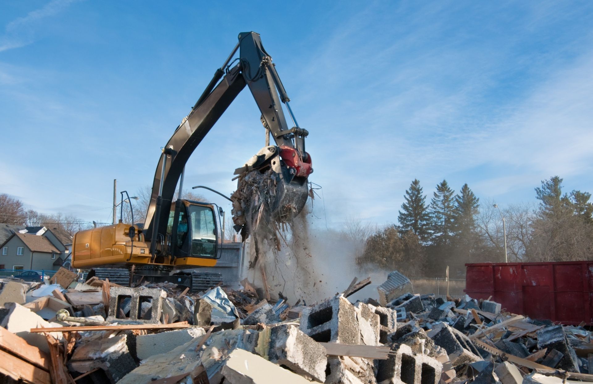 Excavator demolishing concrete rubble at a construction site under a blue sky