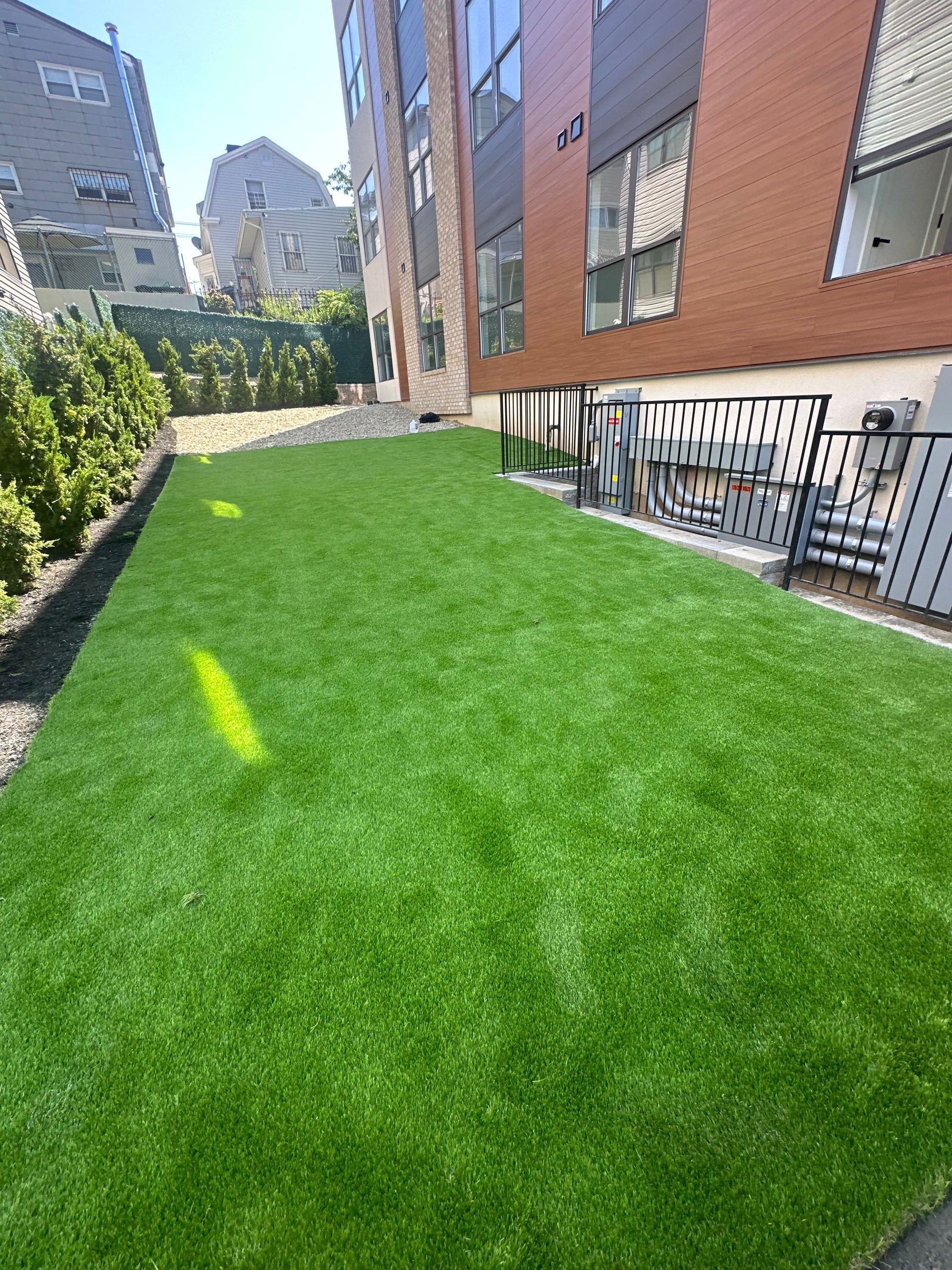 Bright green courtyard lawn beside brick apartment buildings and a black metal fence