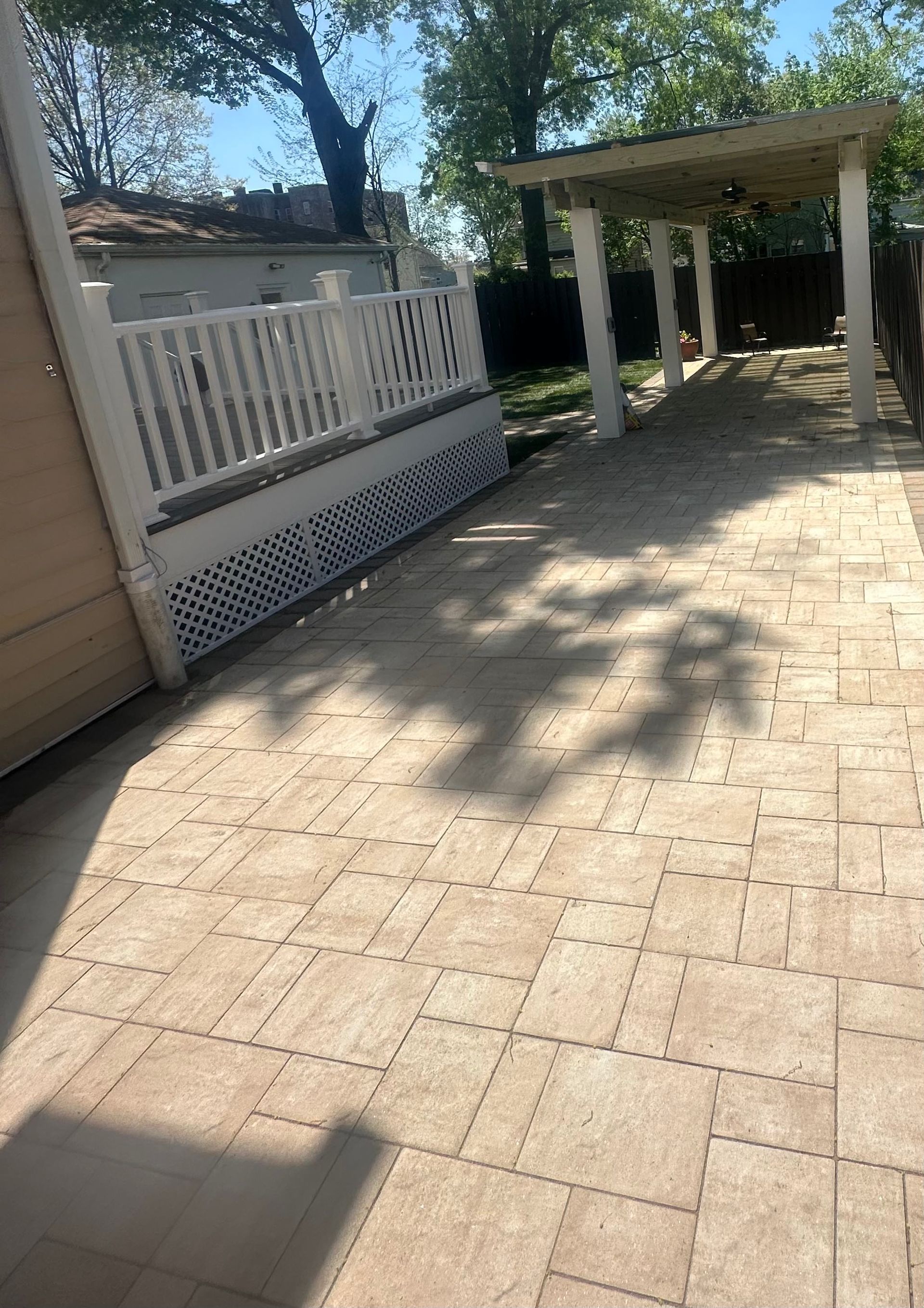 Sunny brick patio with white fence, lattice skirting, and covered walkway beside a house