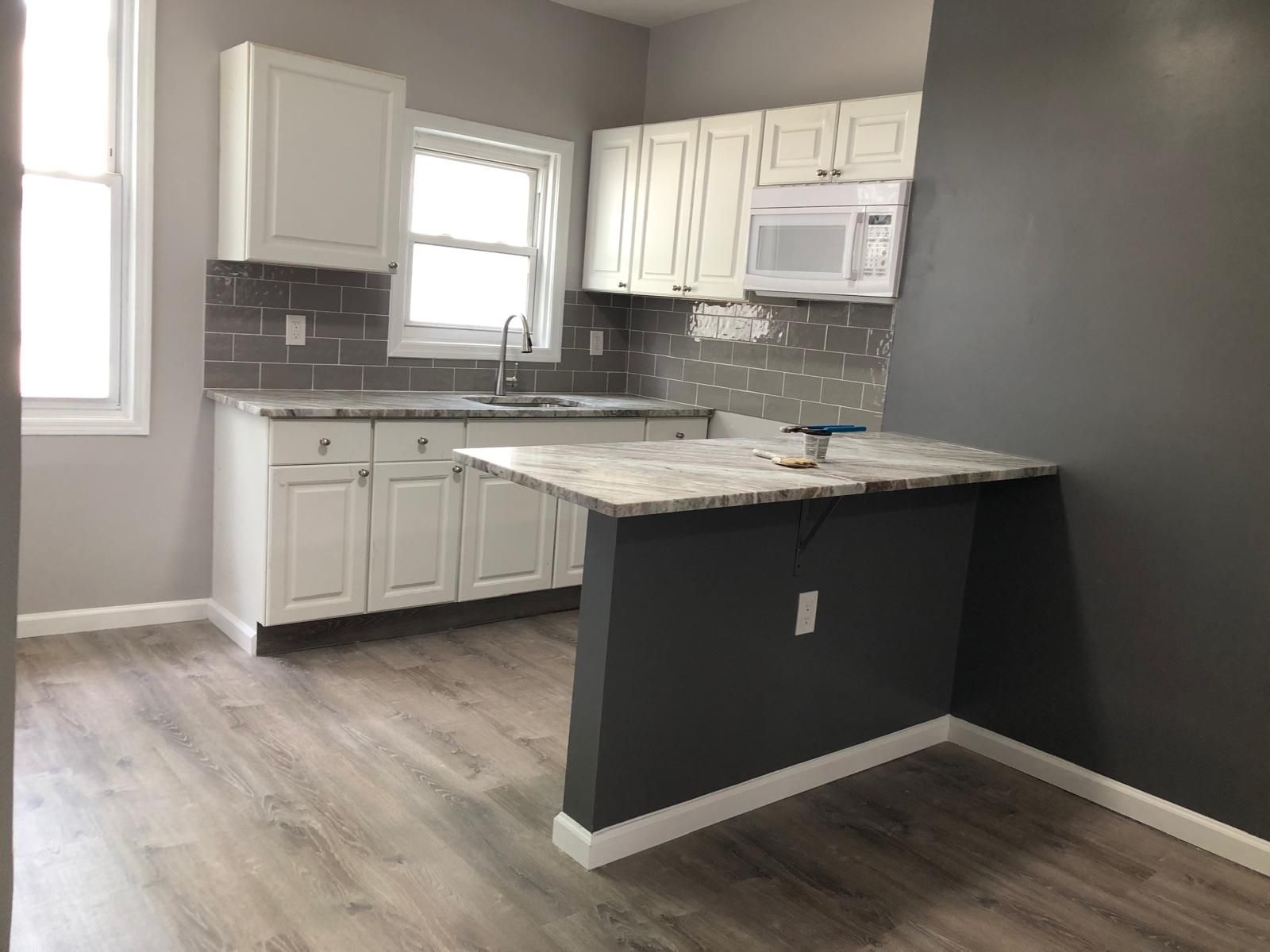 Empty modern kitchen with white cabinets, gray walls, and a marble island countertop