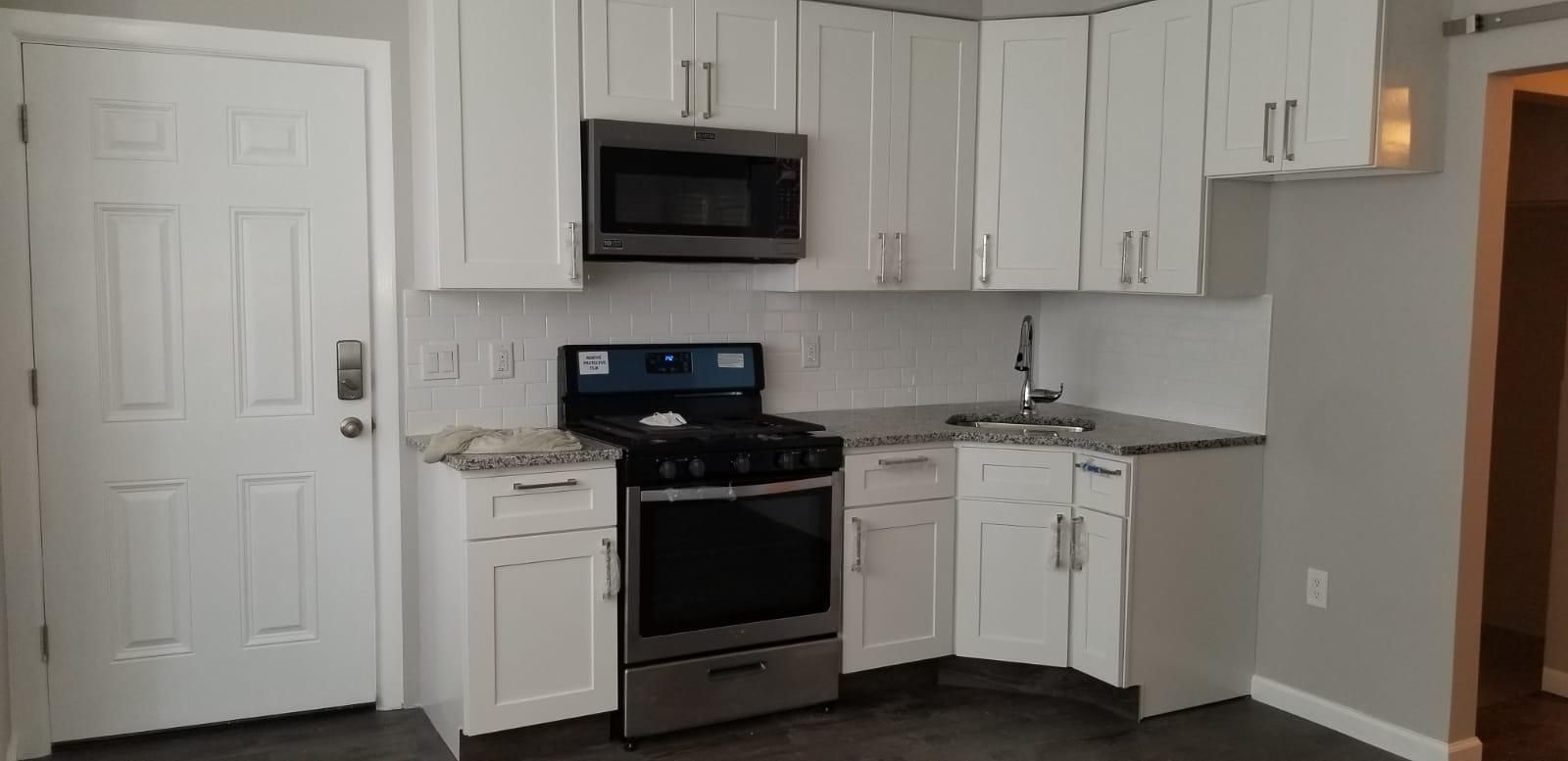 Small white kitchen with black stove, microwave, cabinets, and gray countertops.