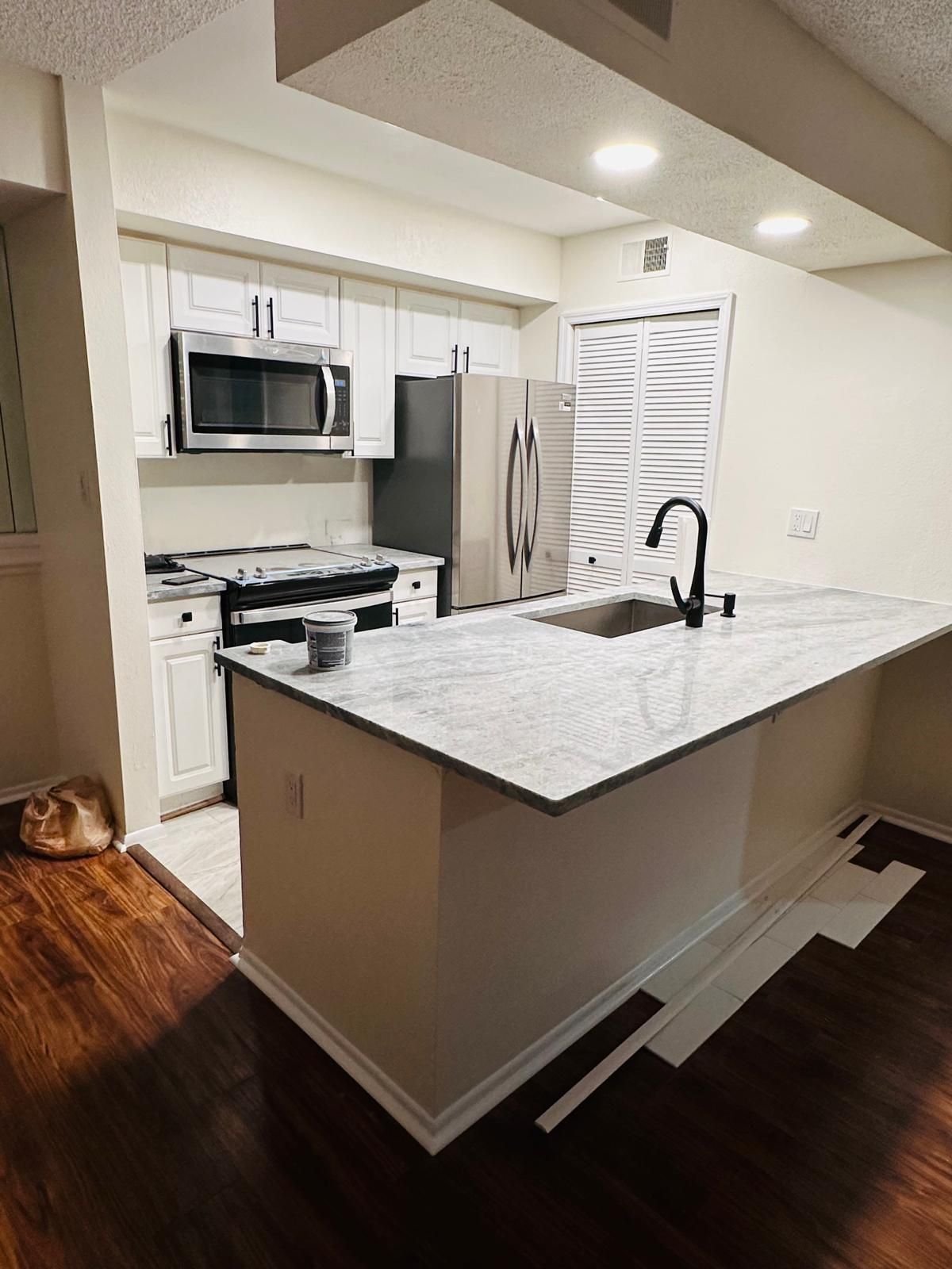 Modern white kitchen with island, stainless steel appliances, dark wood floors, and pendant lights