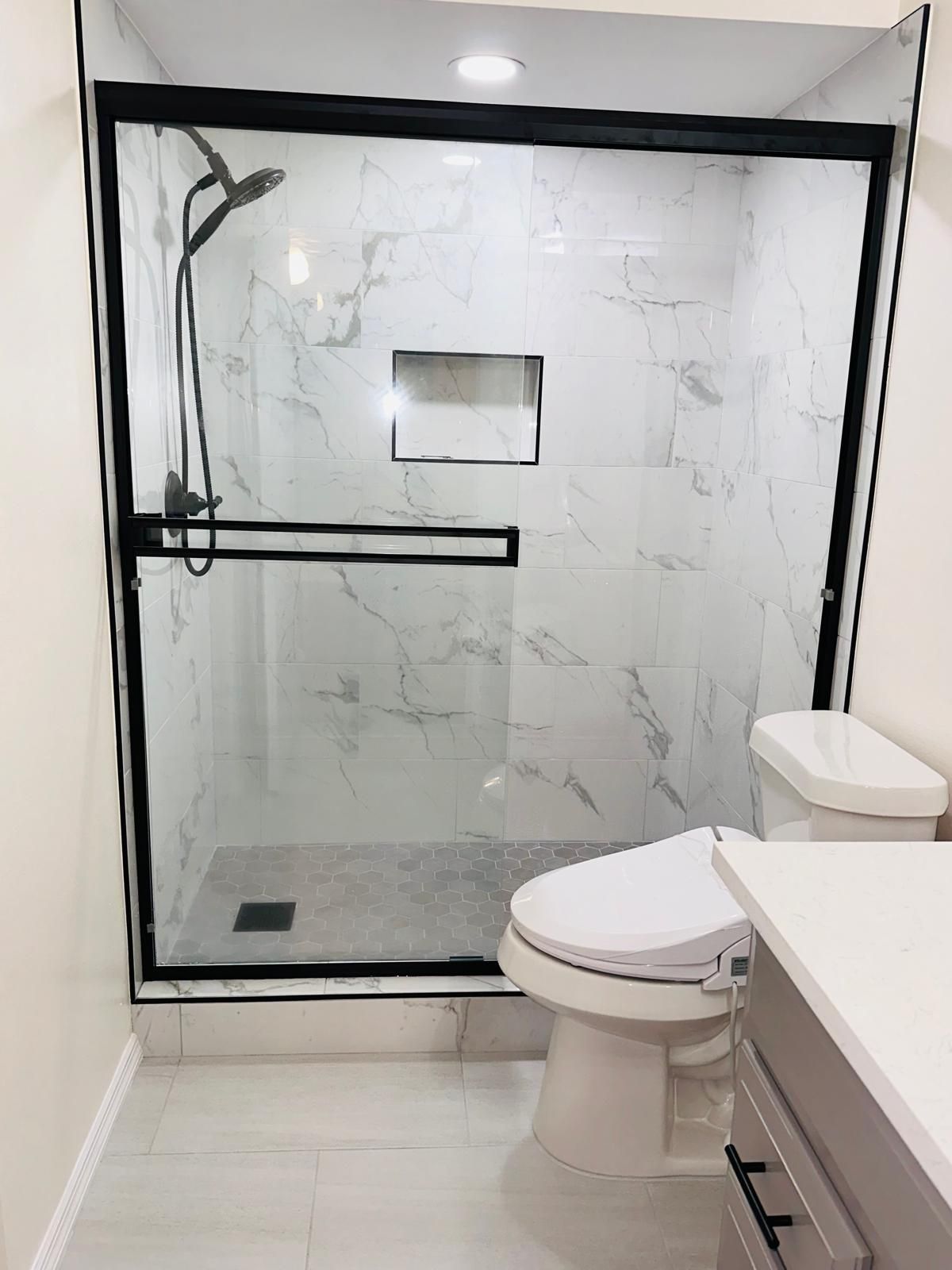 Modern bathroom with walk-in shower, black-framed glass, marble tiles, and a toilet in the foreground