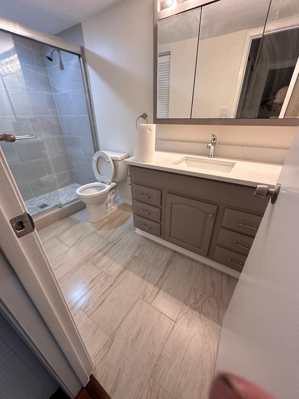 Modern bathroom with gray vanity, large mirror, sink, toilet, and tiled shower stall