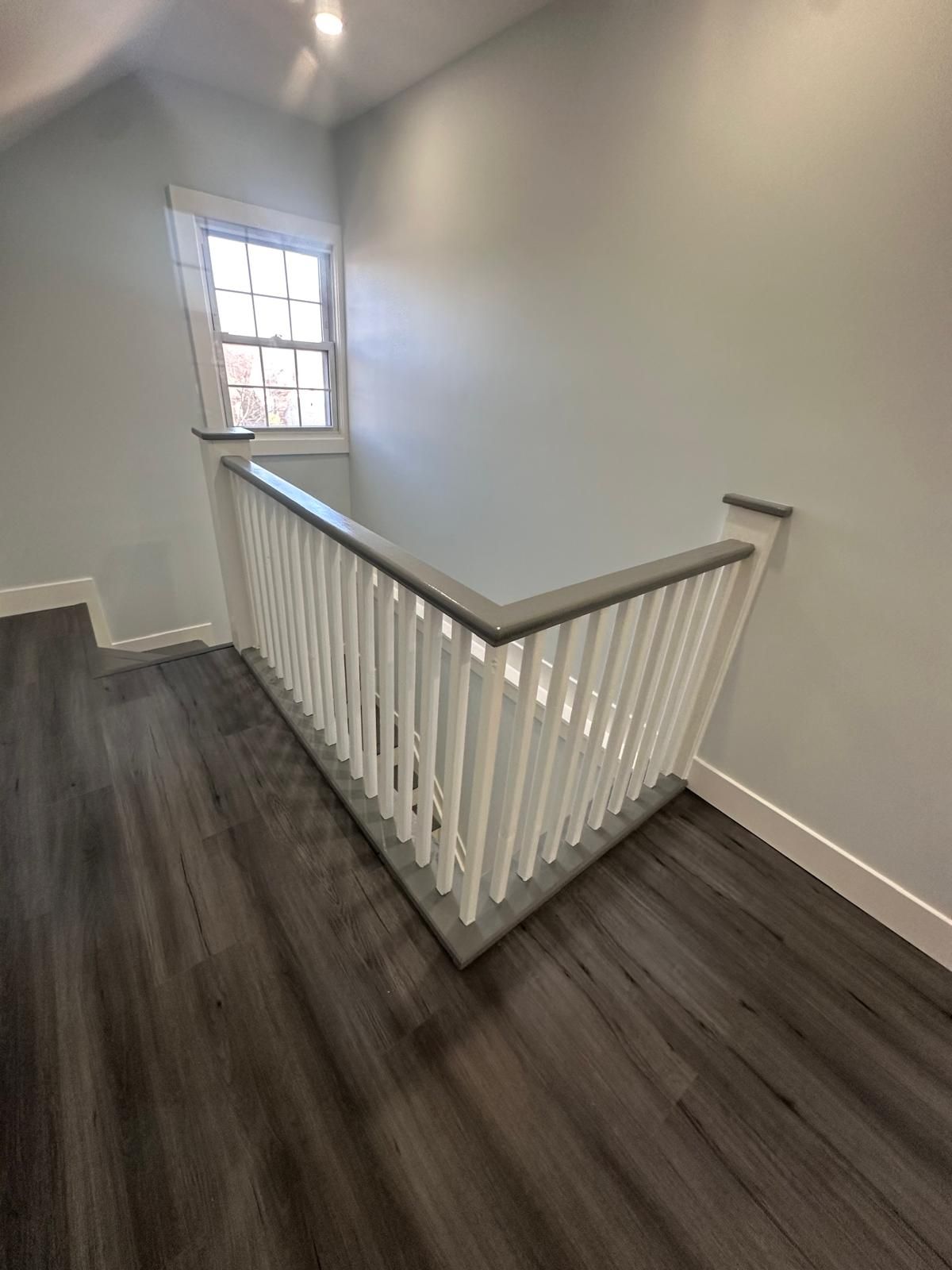 Stair landing with white banister, dark wood floor, and a window letting in daylight