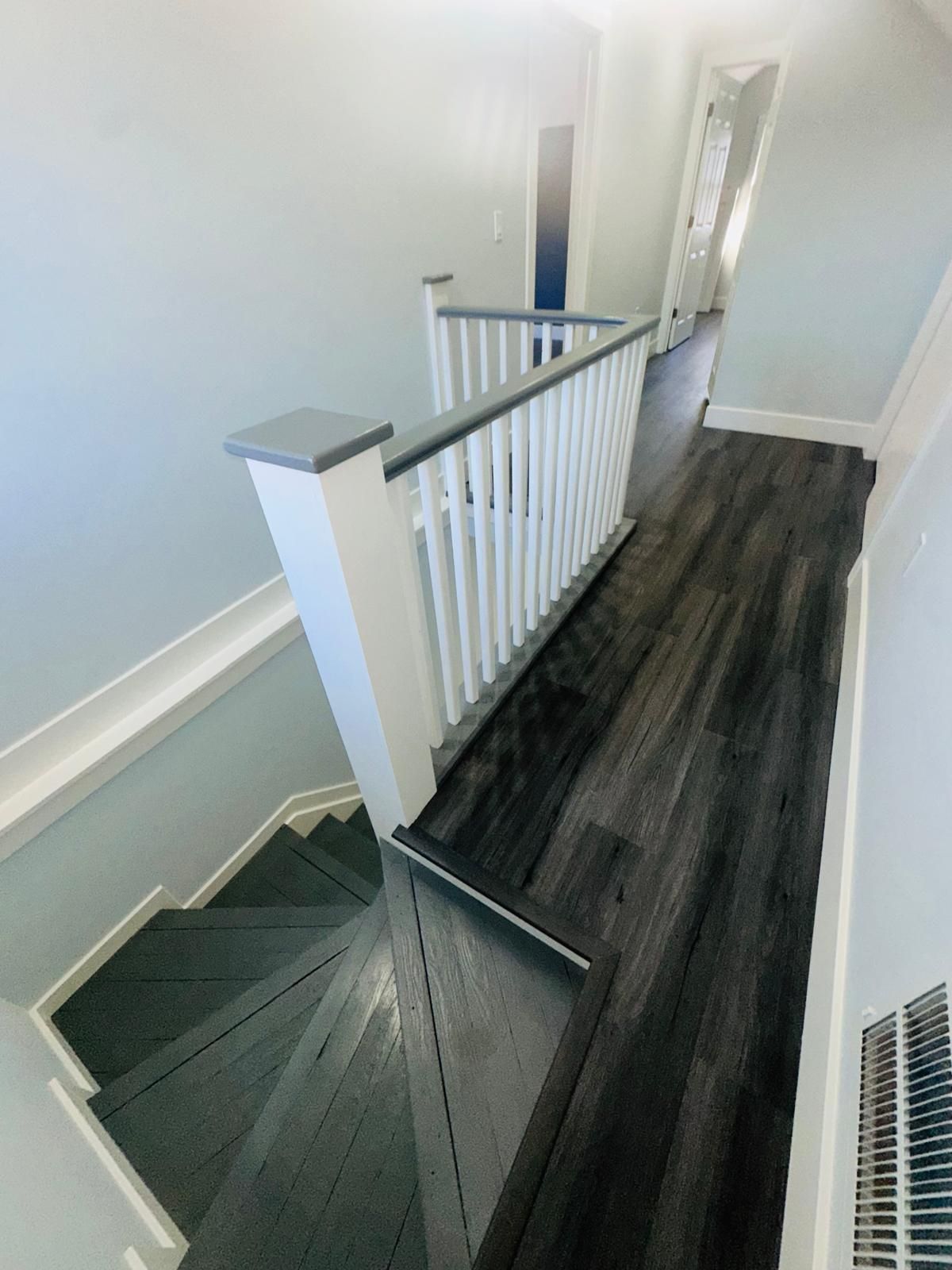 Narrow upstairs hallway with dark wood floor and white railing beside a gray-carpeted staircase