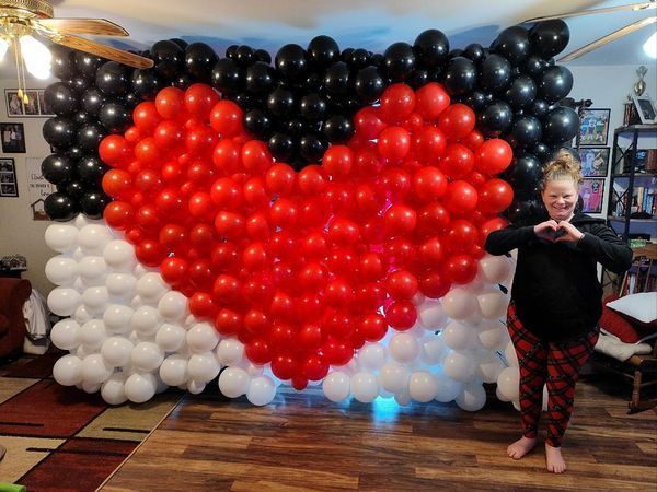 A woman is standing in front of a heart made of red and black balloons.