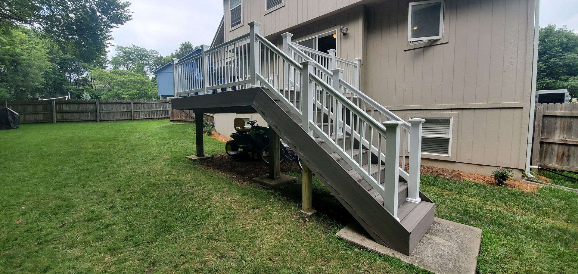 White exterior staircase leading to a raised beige house with a grassy yard and cloudy sky