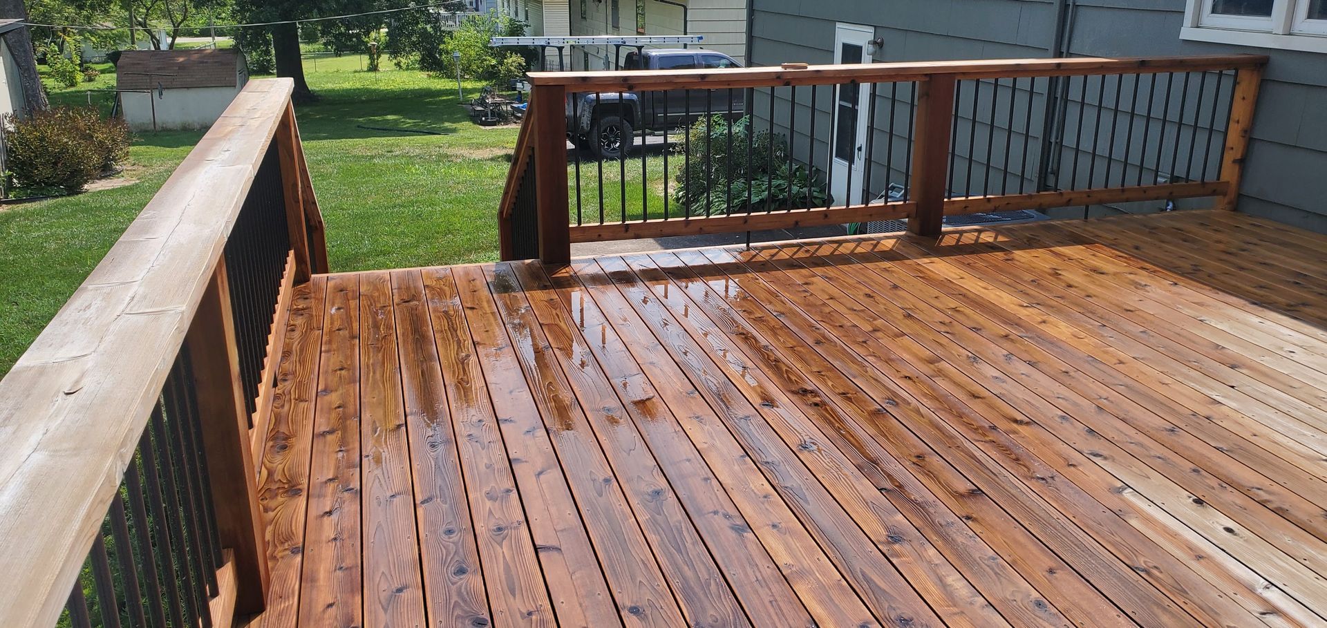 Wet wooden deck with railing and steps in a grassy backyard