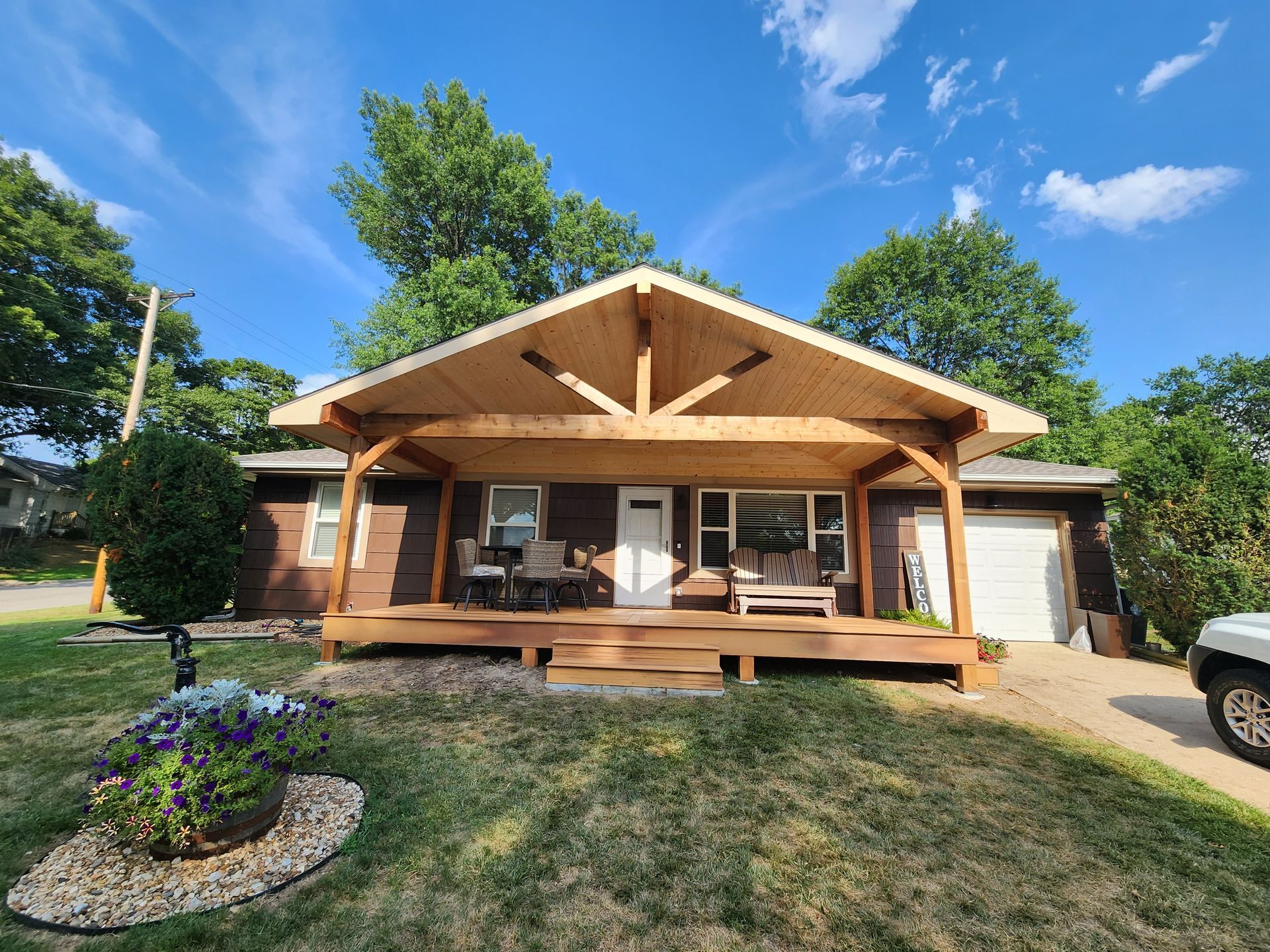 Wooden cabin with a front porch, surrounded by trees and a grassy yard on a sunny day
