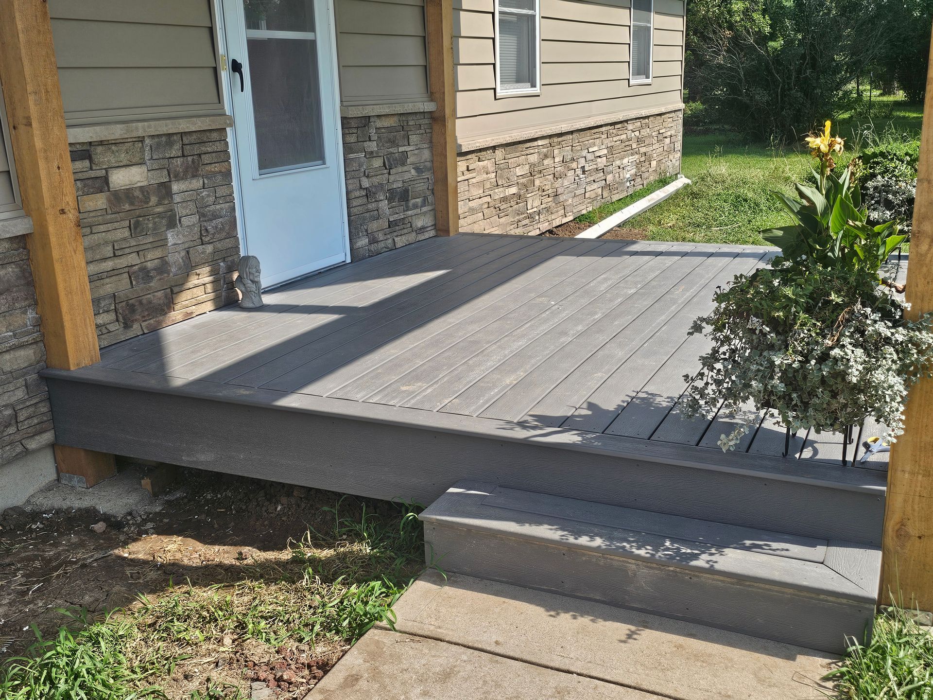 Front porch deck with gray steps, a blue door, and stone siding on a house