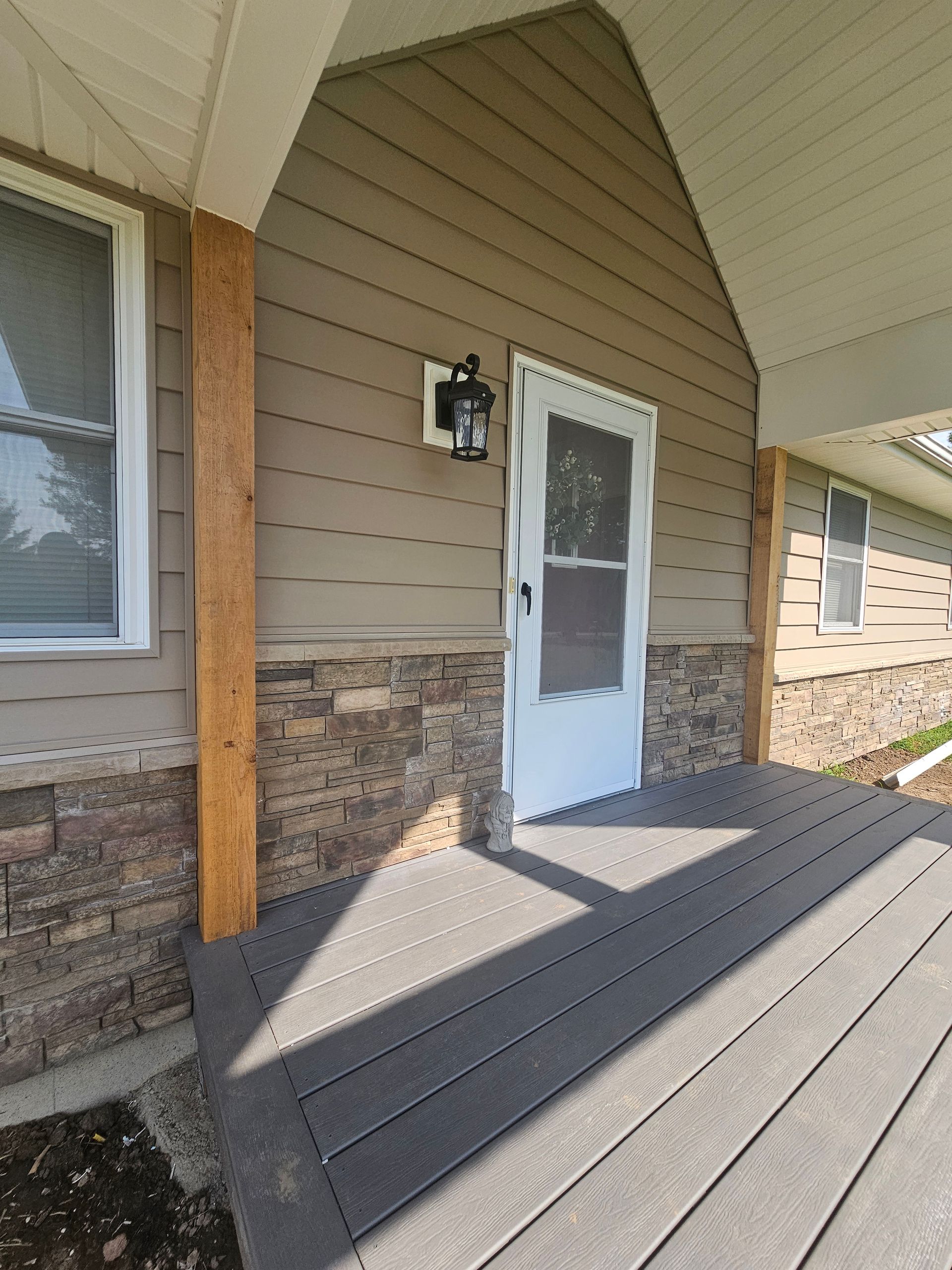 Front porch with white door, tan siding, stone base, and gray wooden deck boards.
