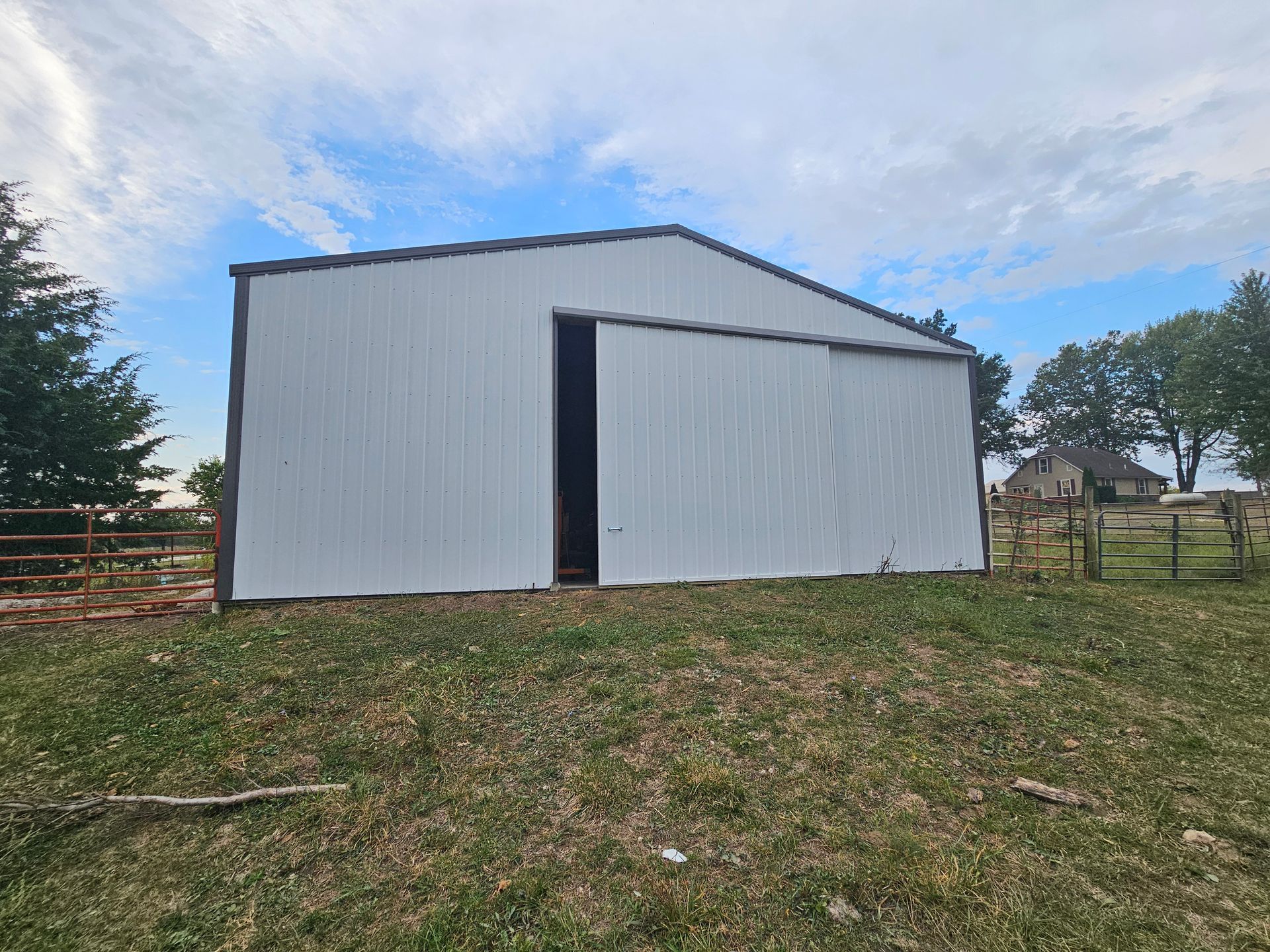 White metal barn with a large sliding door on a grassy hillside under a cloudy sky
