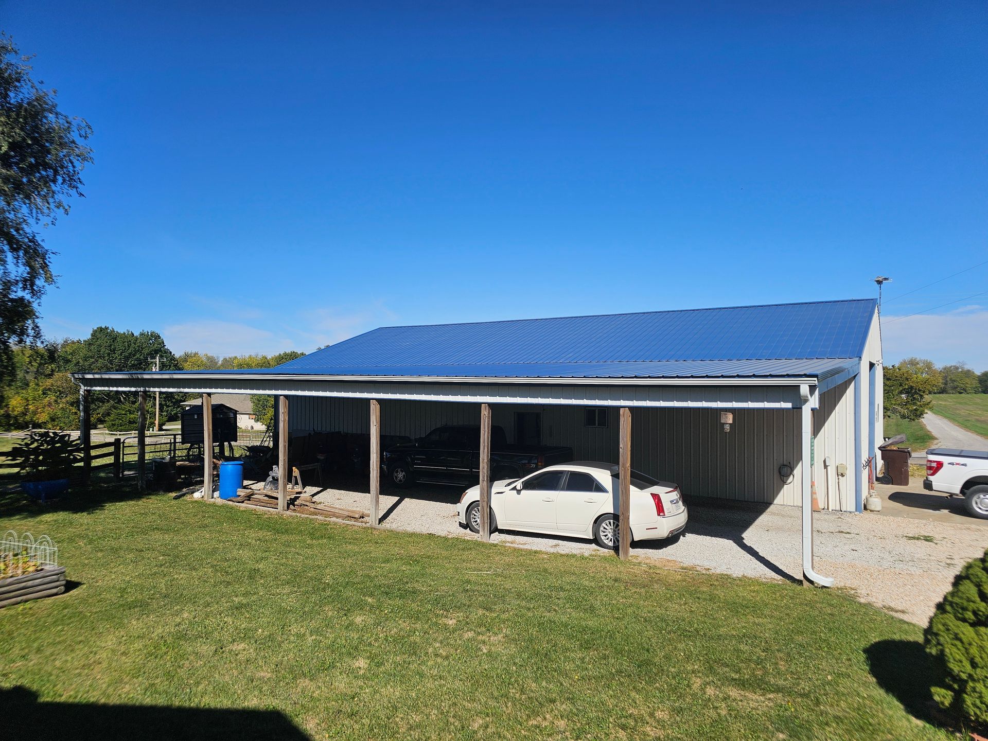 Blue-roofed carport on a grassy hill with a white car parked underneath and open countryside beyond