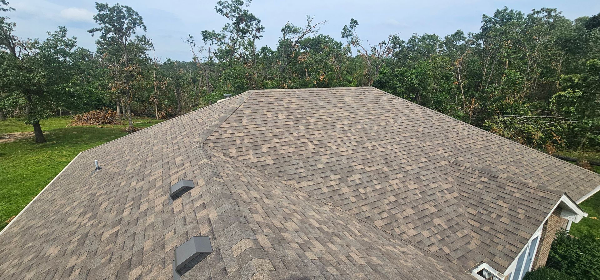 Roof with gray shingles and two vents, seen from above against trees and sky.