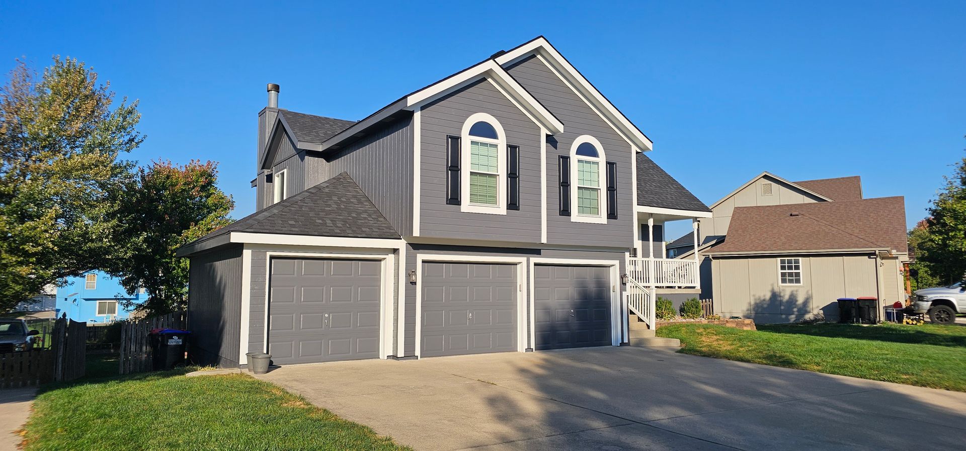 Gray two-story suburban house with a three-car garage and a driveway on a sunny day