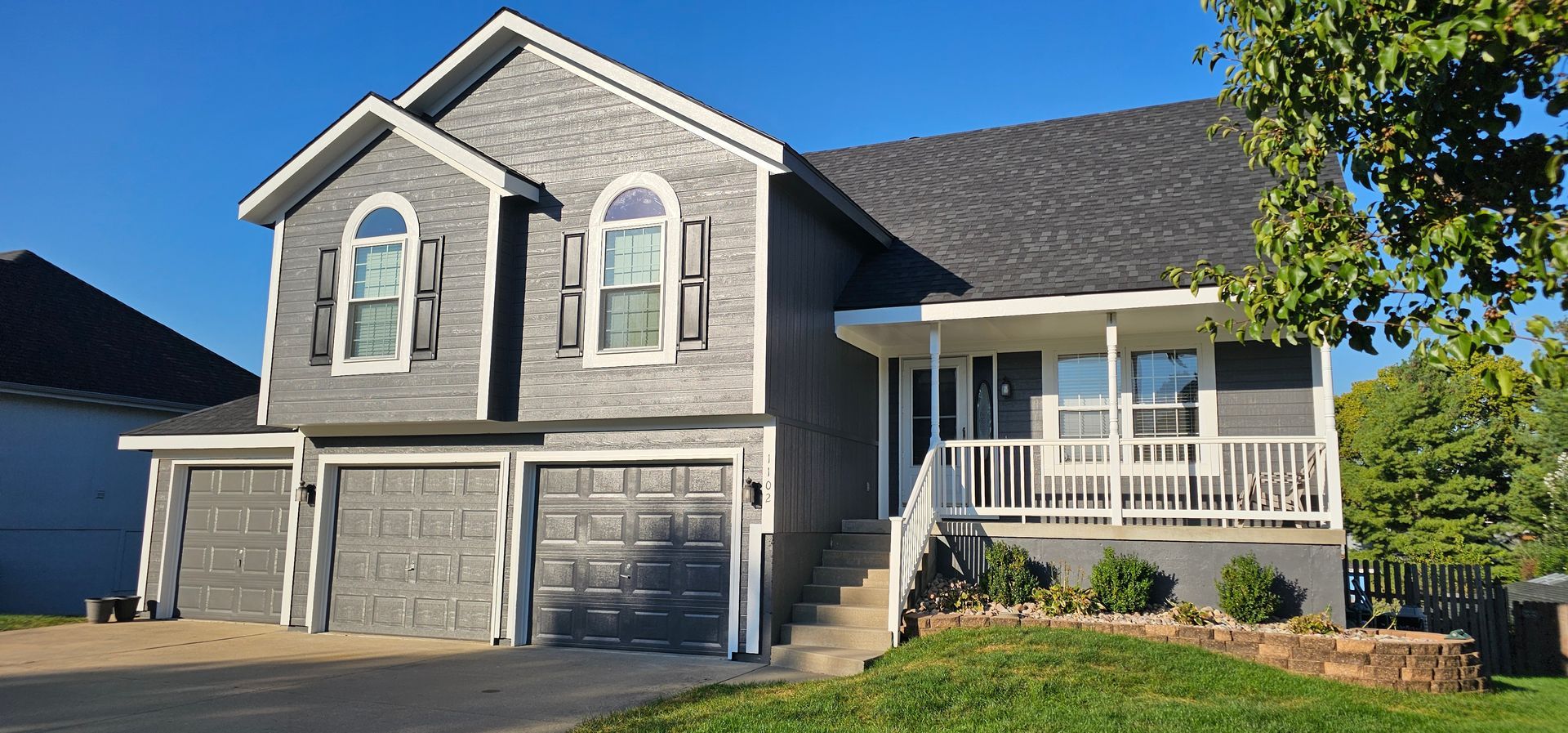 Two-story gray house with a white porch, double garage, and blue sky