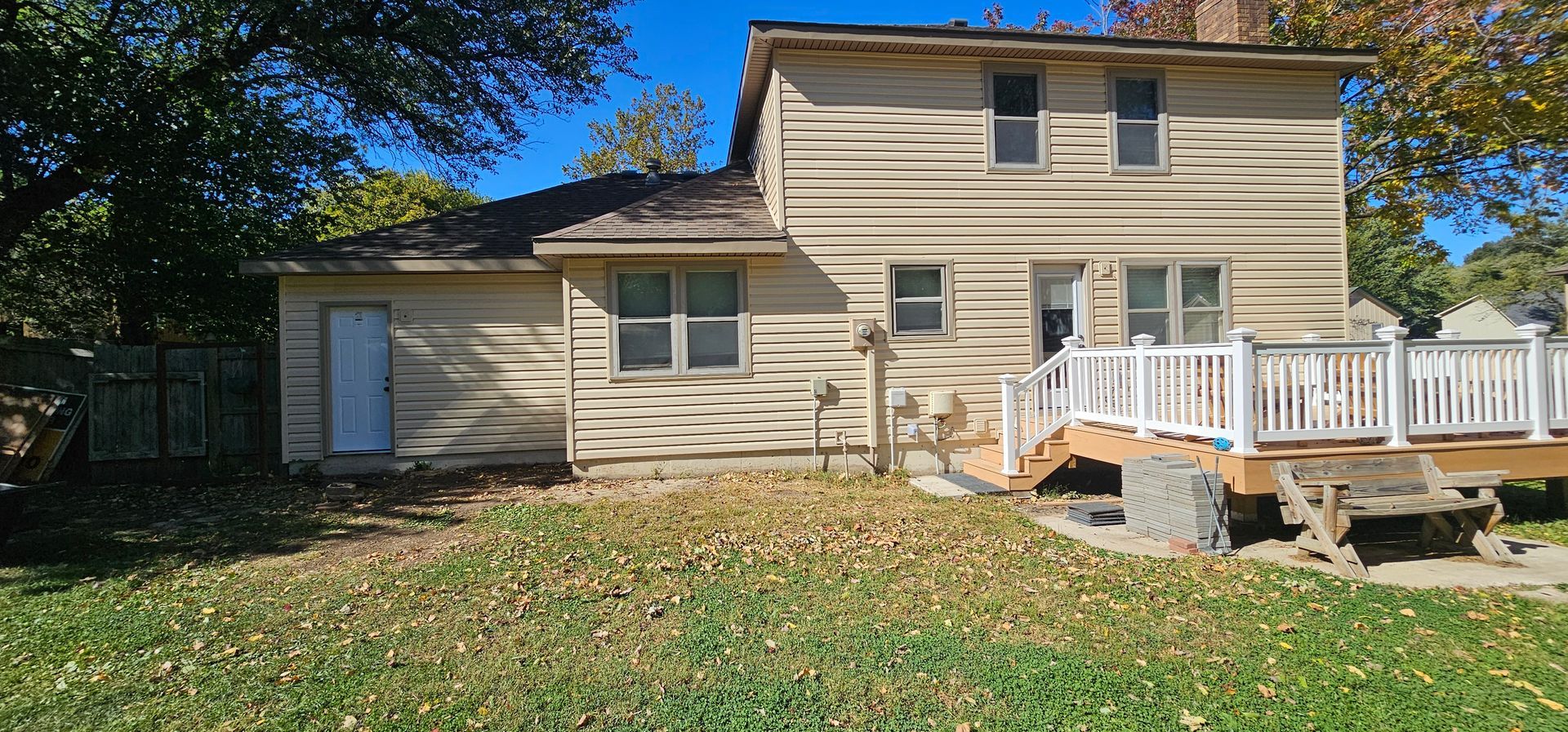 Beige two-story house with attached garage and white porch, seen from the yard in daylight