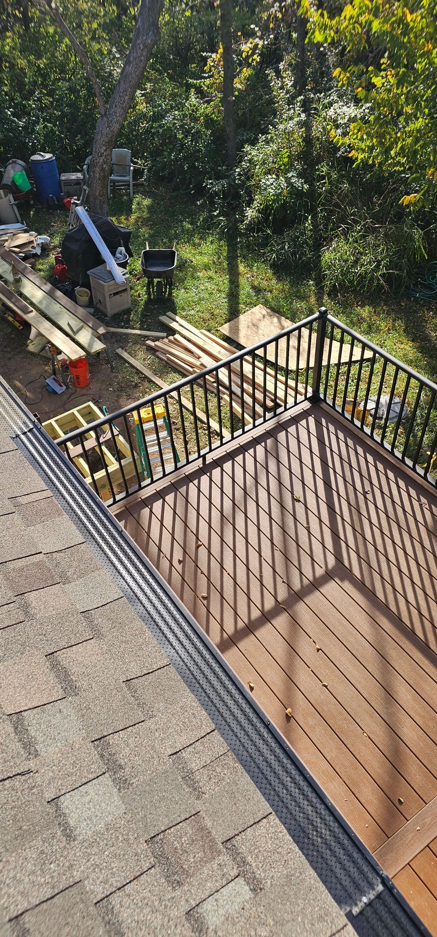 Backyard patio with stairs, black railing, tan stone tiles, and a wooden deck overlooking a garden