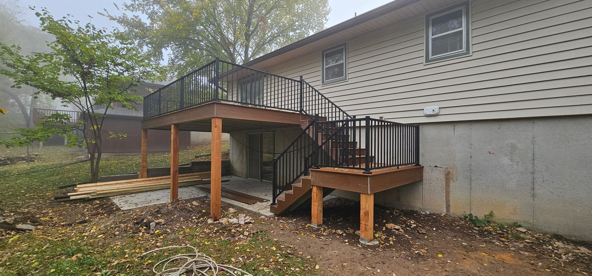 Covered wooden wheelchair ramp and stairs beside a beige house with leaf-covered ground