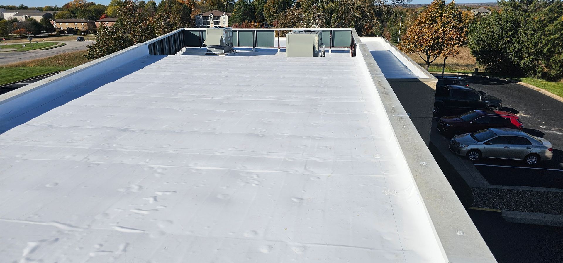 White flat rooftop with HVAC units and parked cars visible below on the right.