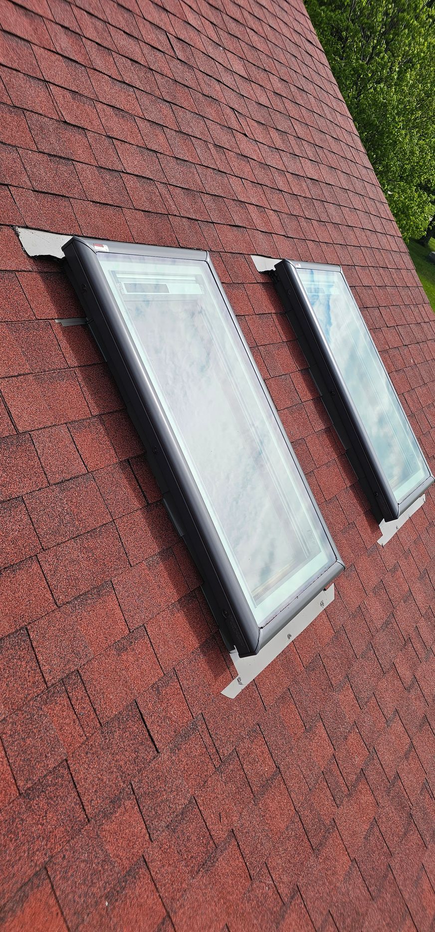 Two skylights on a red shingle roof, viewed at an angle.