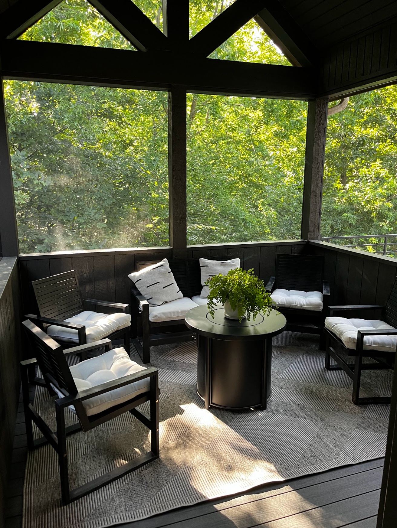 Sunlit screened porch with black wicker chairs, white cushions, and a round table with flowers