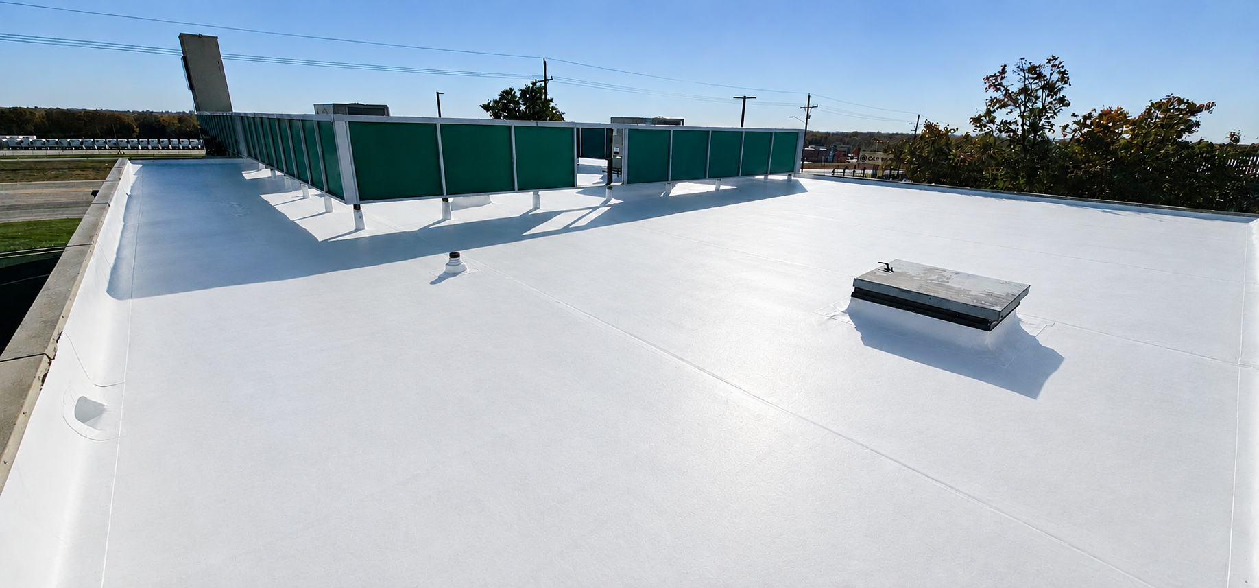 White flat rooftop with teal safety barriers and a small skylight under a clear sky