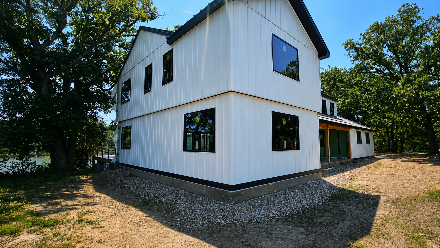 White two-story house with black-trimmed windows, a gravel driveway, and trees in the yard
