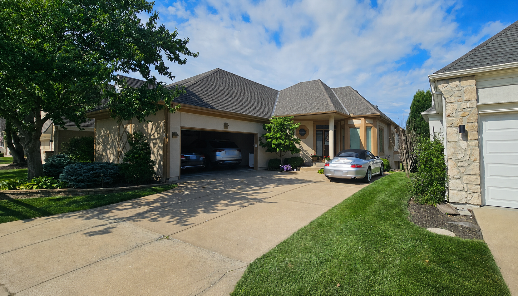 Suburban house with open garage, driveway, parked car, and green lawn under a blue sky